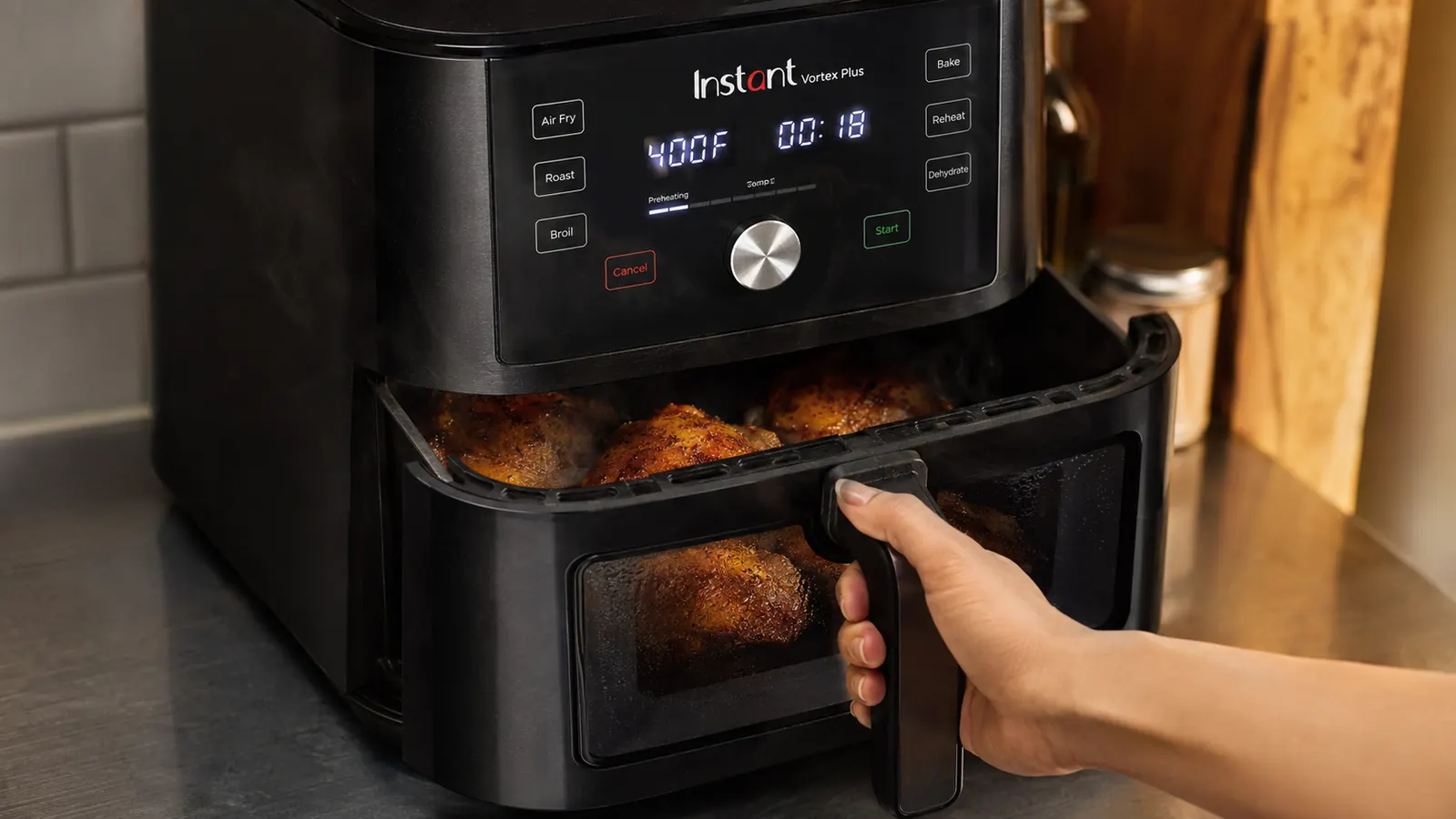 A hand pulling open the air fryer basket drawer to check crispy chicken thighs through the clear window