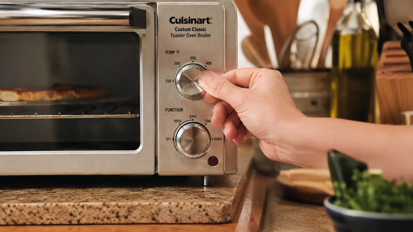 A hand turning the manual temperature dial on the front of the toaster oven