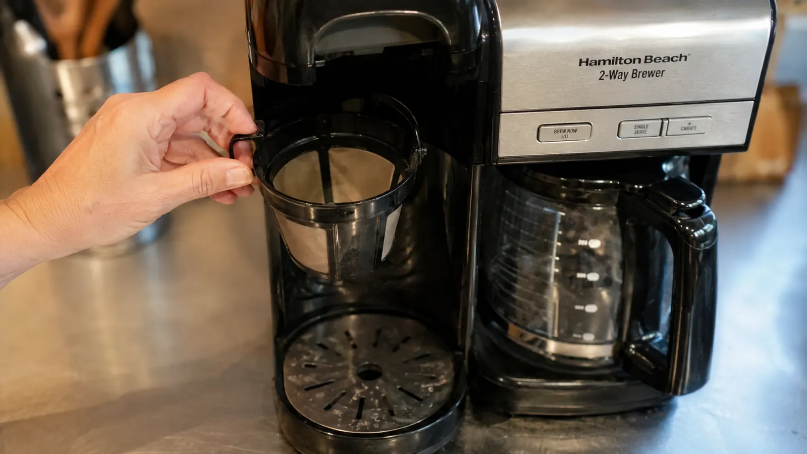 A hand lifting the reusable single-serve filter basket out of the coffee maker to check for grounds buildup