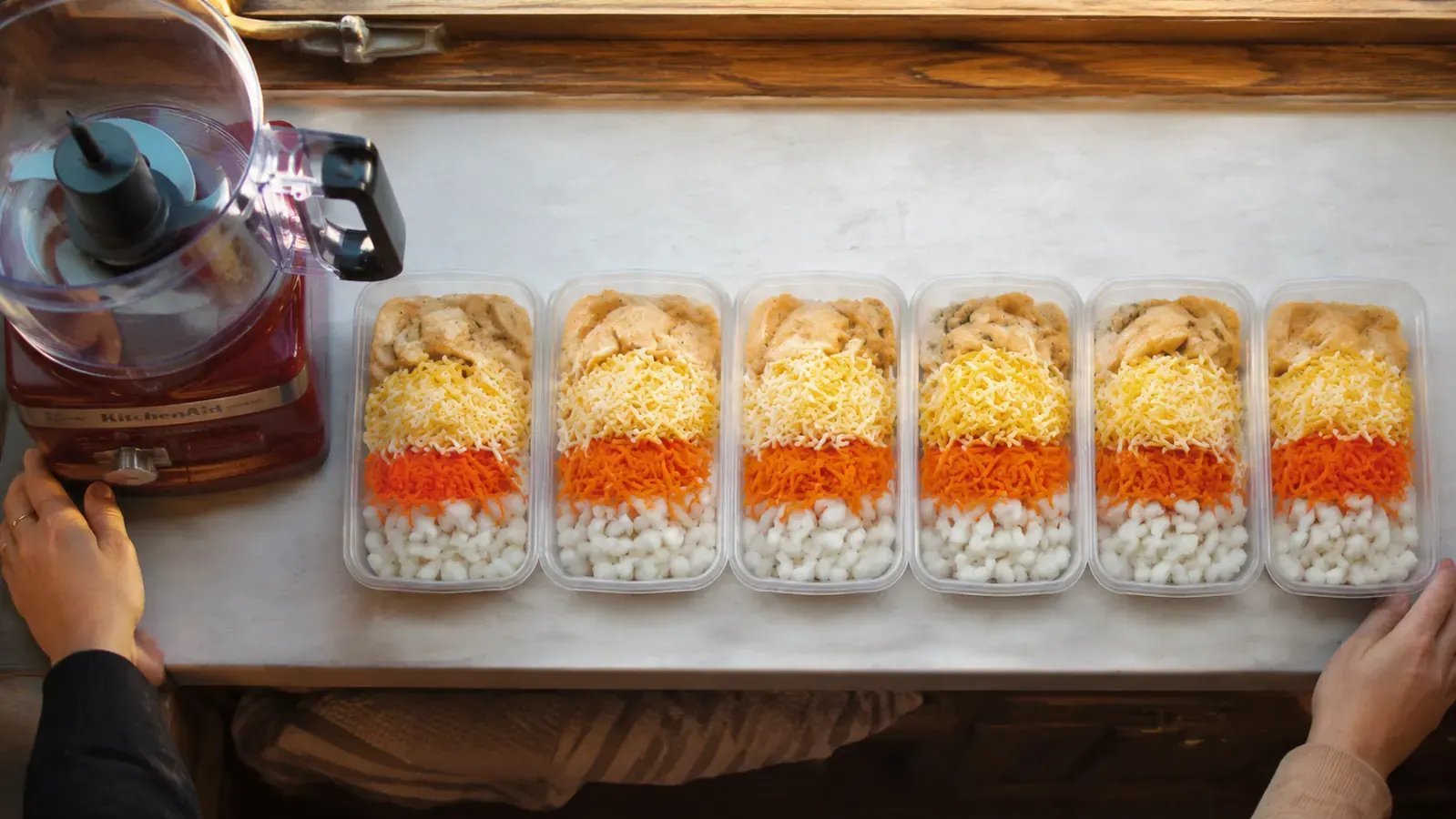 Six labeled meal prep containers lined up on a small kitchen counter ready for the fridge