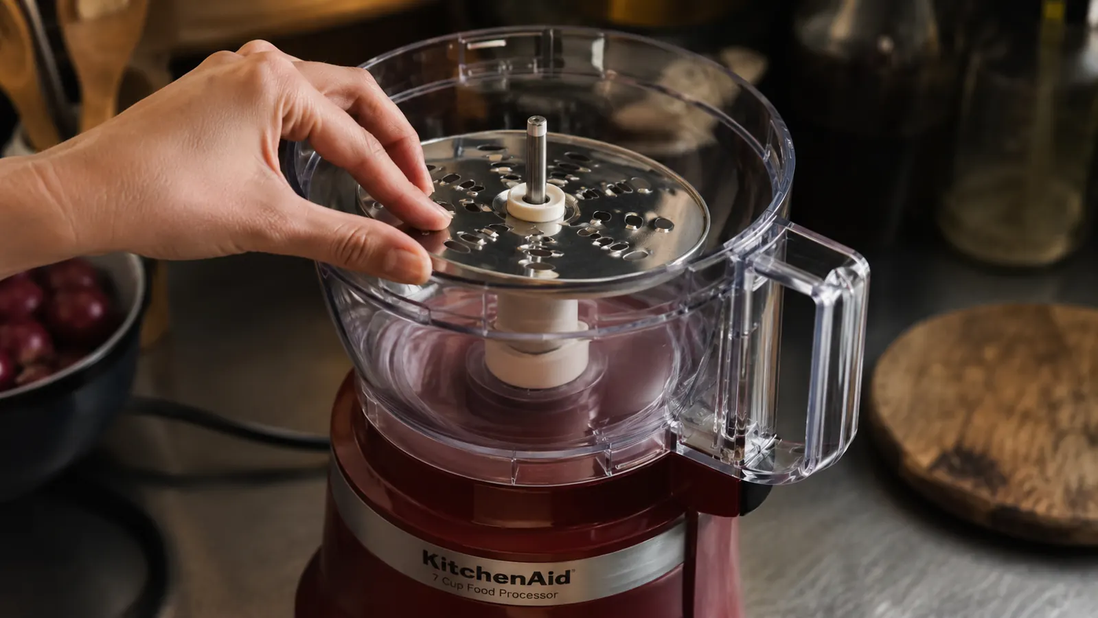A hand carefully locking the shredding disc onto the drive shaft of the food processor bowl